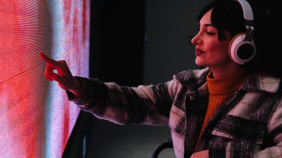 Woman in wheelchair reaching out to touch a colorful digital screen at an interactive art exhibit.