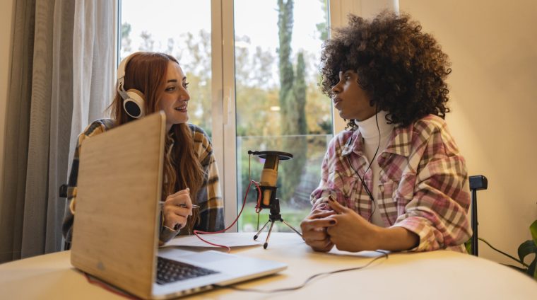 Duas pessoas conversando diante de microfones em um estúdio